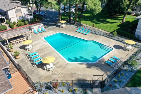 Drone photo of the community swimming pool area which is fenced and pool deck is filled with seating options. at Renaissance Park Apartments, Davis, CA, 95618