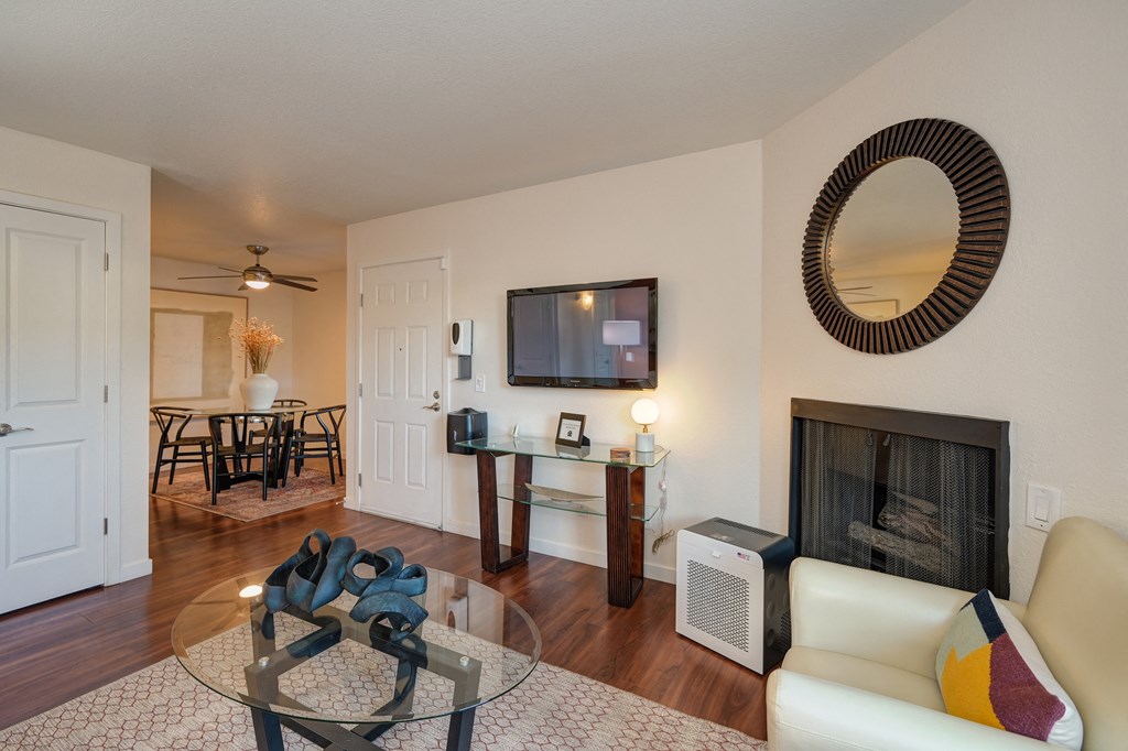 Living Room with Hardwood Inspired Floor, Rug, Glass Table, Round Mounted Mirror above fireplace, and Flat Screen Television above entry table