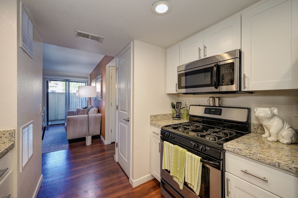 Model home kitchen with gas stove and microwave above the stove. Granite countertops and hardwood inspired flooring.