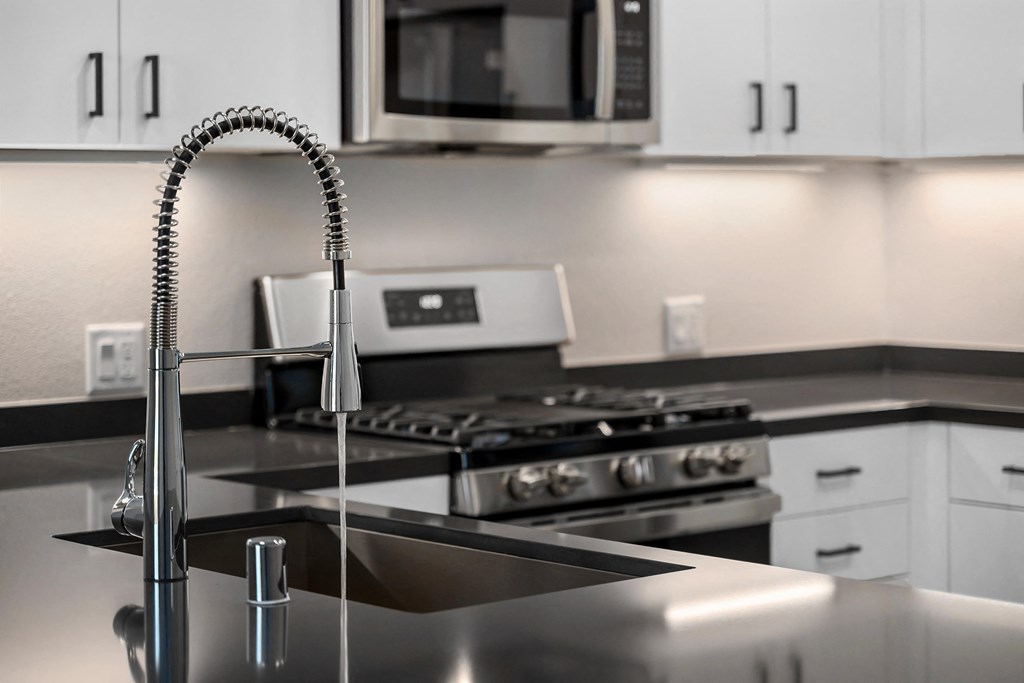 a kitchen with a sink with a gooseneck style faucet with water turned on and a stove in the distance at Sierra Gateway Apartments, Rocklin, CA, 95677