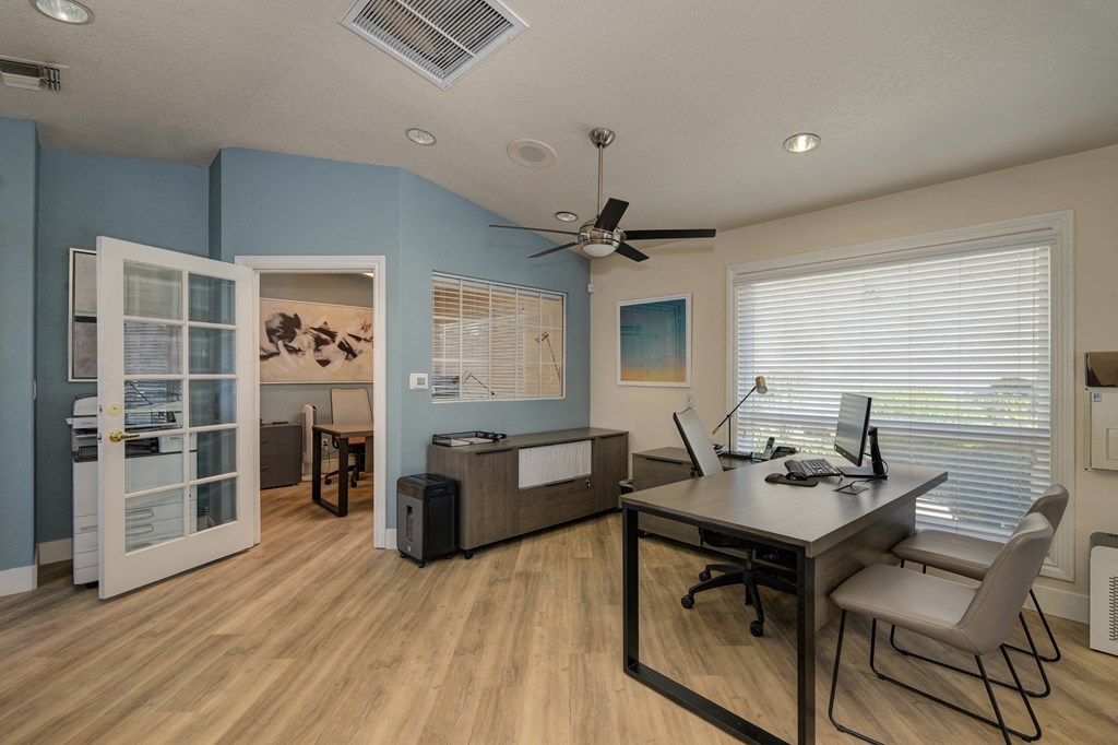 The Legacy Leasing office with large desk and chairs for meeting with prospective renters.  Office has light colored wood flooring and a light blue accent wall. at The Legacy Apartments, California