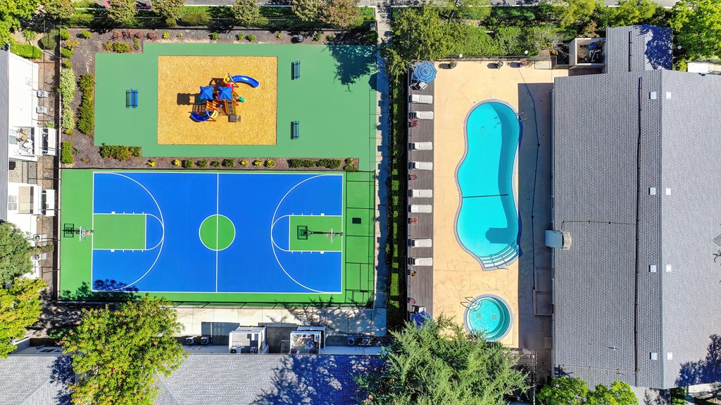 A basketball court is surrounded by a pool and a playground.