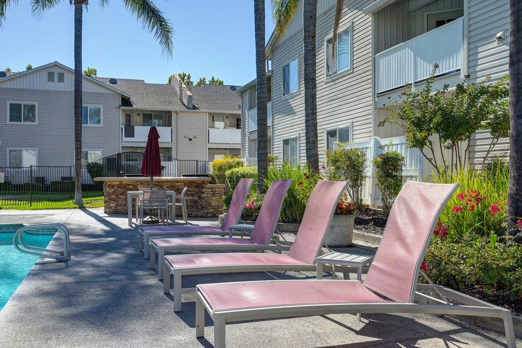 a group of lounge chairs lined up on the pool deck next to a pool at The Legacy Apartments, Antelope, 95843