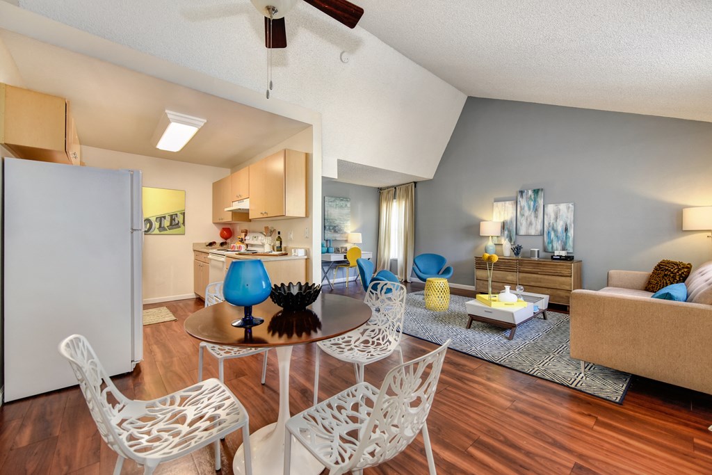 Living Room with View of Kitchen with Hardwood Inspired Floor, White Sofa, Rug and Blue Chairs at Vineyard Terrace Apartments, Napa