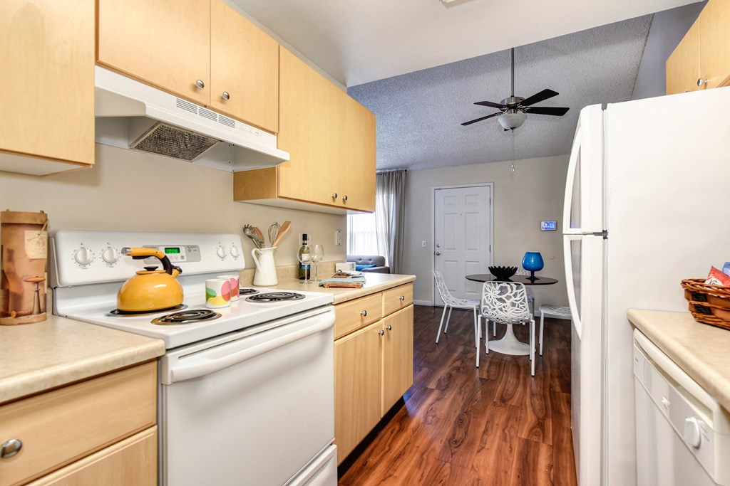 Model home kitchen with hardwood inspired flooring , white kitchen appliances, and dining area with ceiling fan at Vineyard Terrace Apartments, California