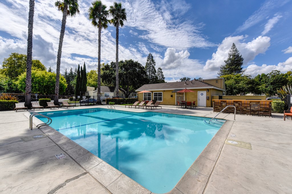Community swimming pool area and sun deck with mature palm trees in the distance Community swimming pool area and sun deck with mature palm trees in the distance at Vineyard Terrace Apartments, California
