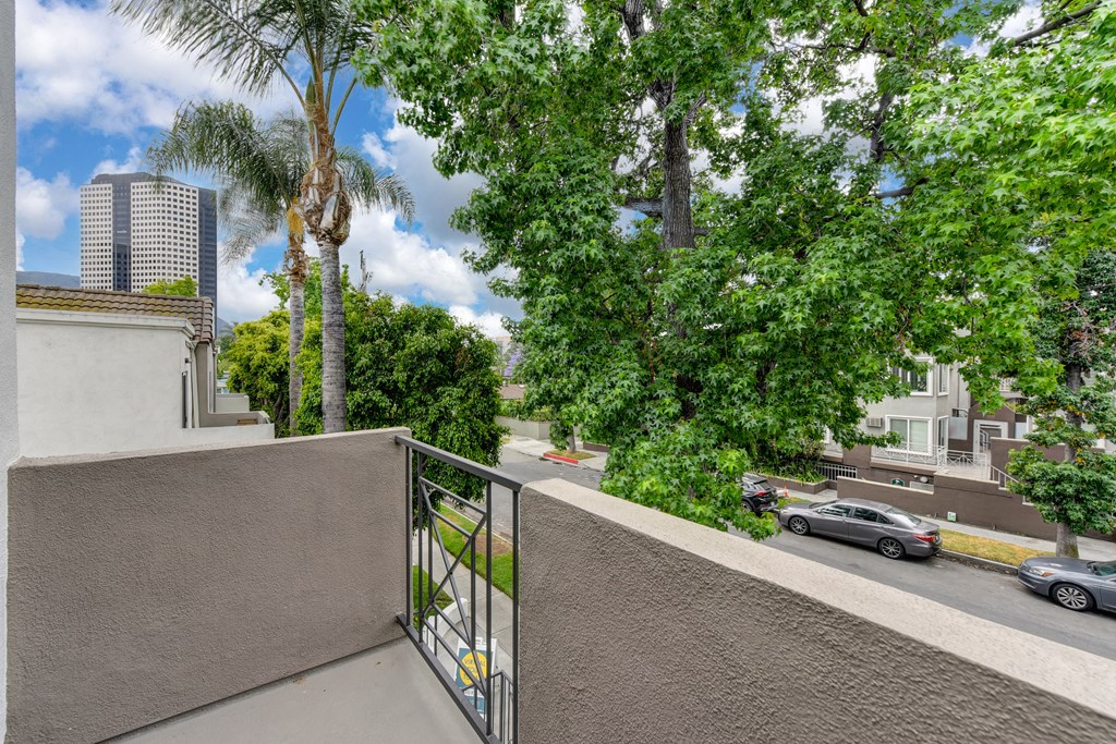 Second floor private patio overlooking the entrance and street in front of the community. There are several mature trees and blue skies. 