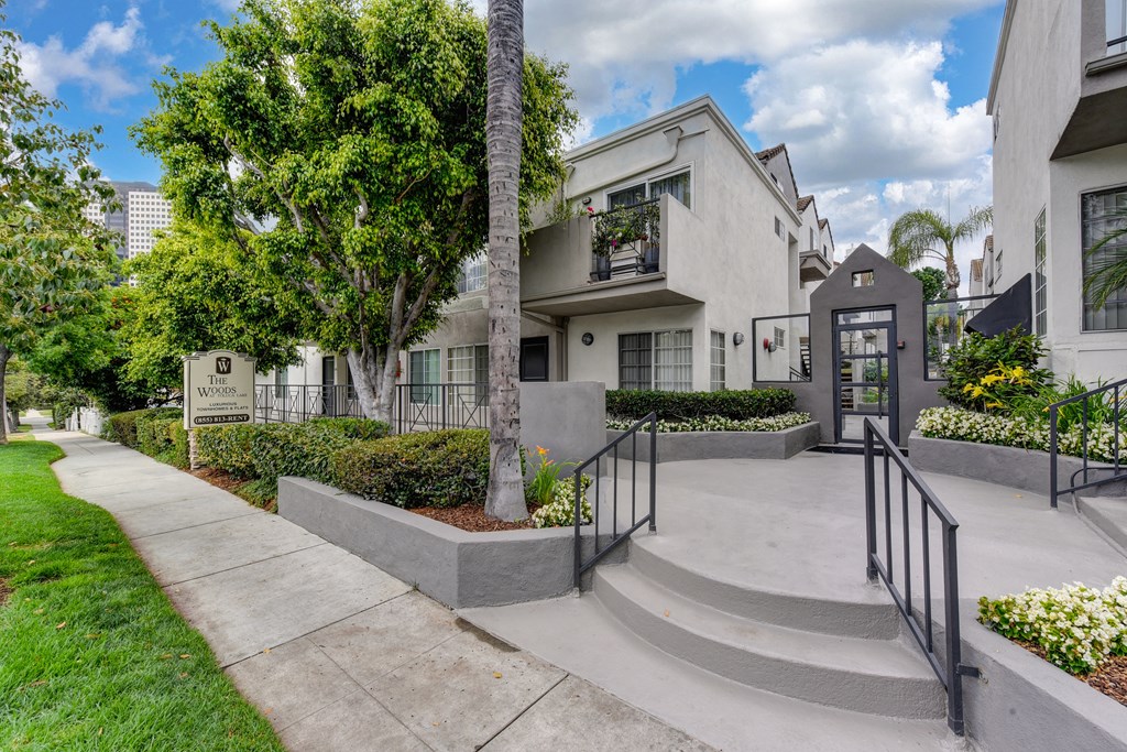 Apartment complex entry from the street.  Palm and other mature trees in front of the apartment complex. 