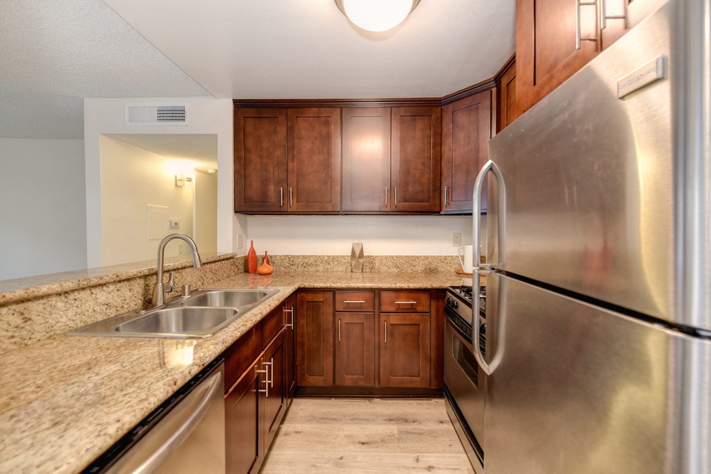 Kitchen area with granite counters, darker cabinetry, stainless  appliances, sink and raised counter for bar top seating.