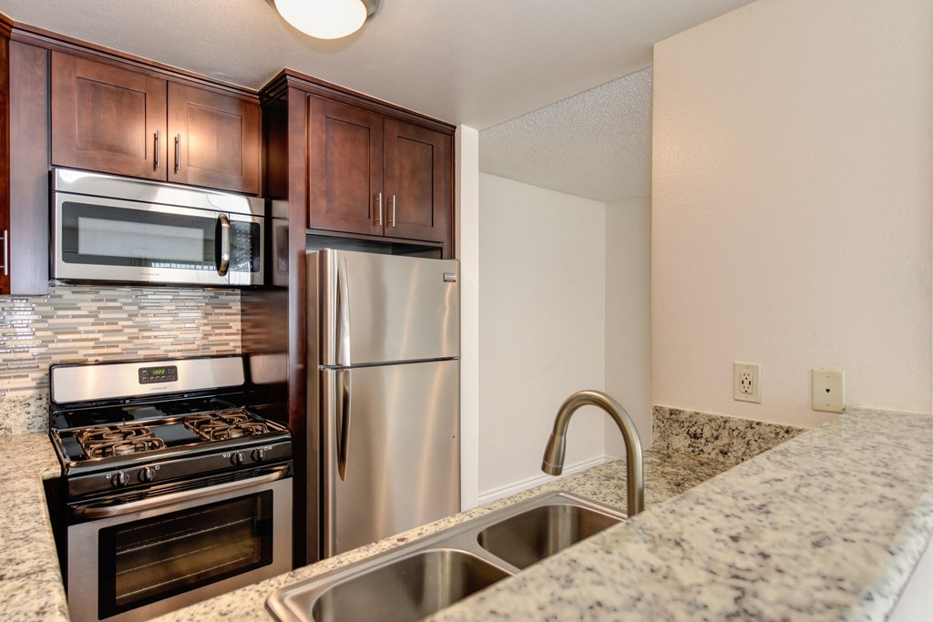 Kitchen area with granite counters, darker cabinetry, stainless  appliances, sink and raised counter for bar top seating.