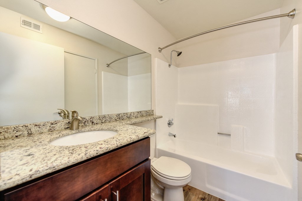 Apartment home bathroom with granite counters, darker cabinetry, toilet and tub/shower enclosure. 