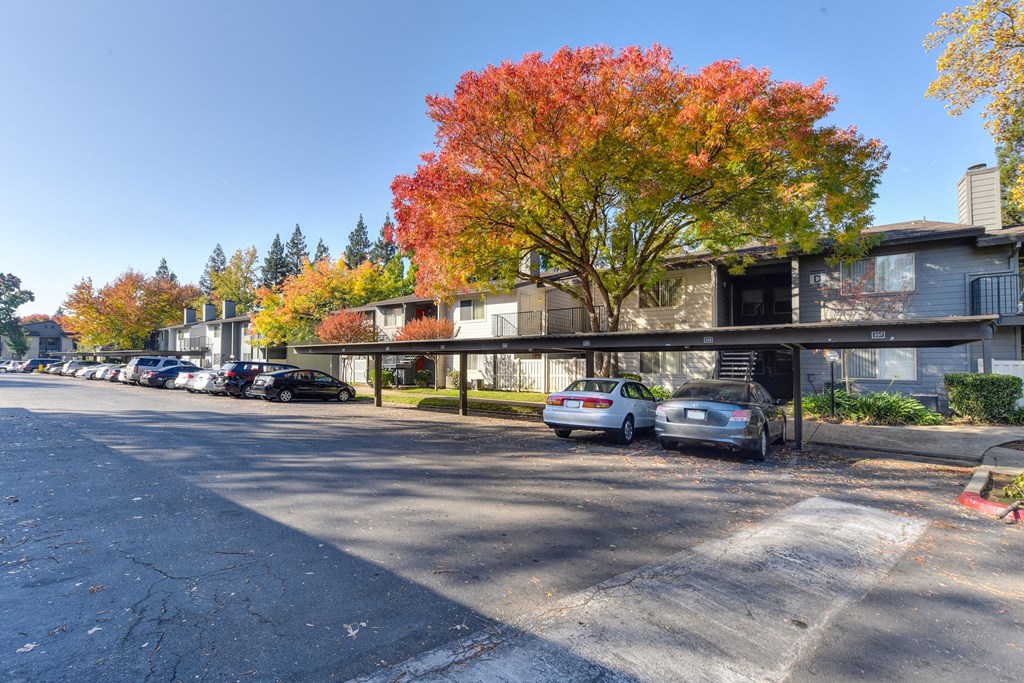 a row of apartment buildings with cars parked in front of them under covered carports