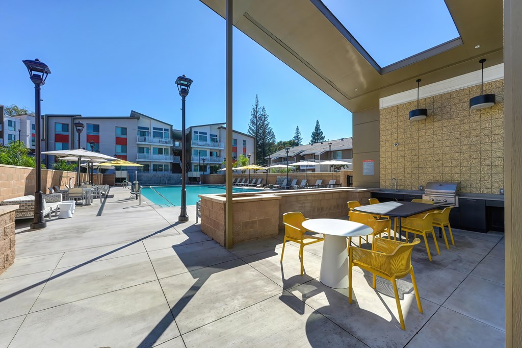 A sunny day at the poolside with yellow chairs and tables.