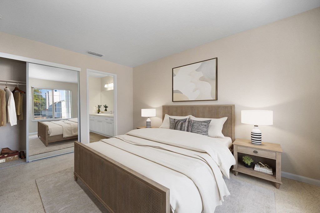 a bedroom with a large bed and a closet with mirrored doors and bathroom attached.