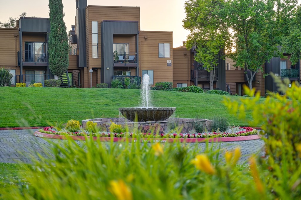 A fountain in the middle of a garden in front of apartment buildings.