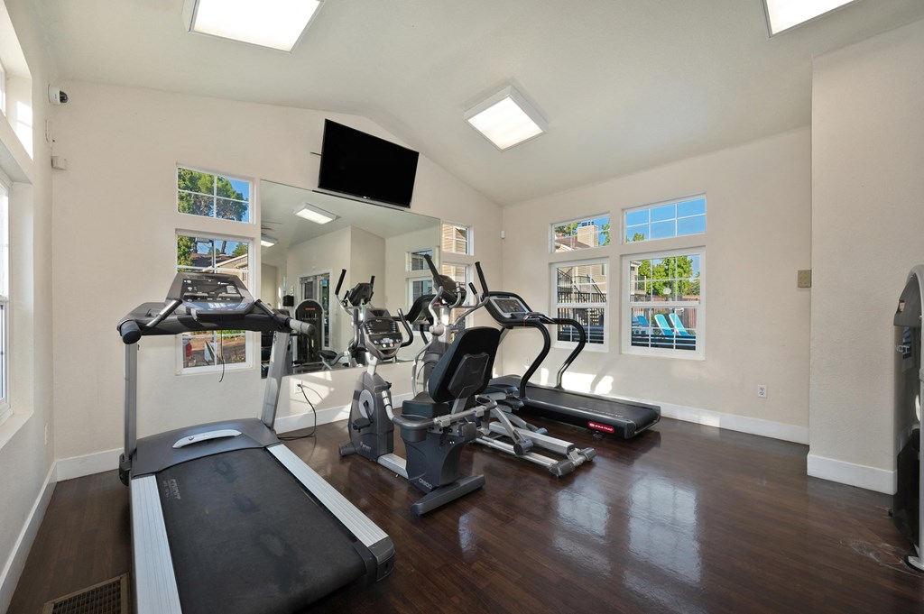 the gym has plenty of exercise equipment and a flat screen tv at Hidden Oaks Apartments, Citrus Heights, 95621