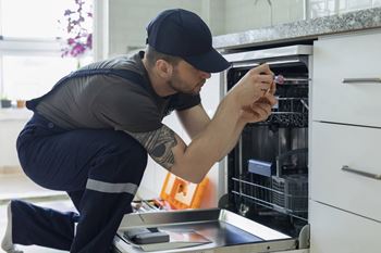 A man in a grey shirt and blue pants is fixing an oven.