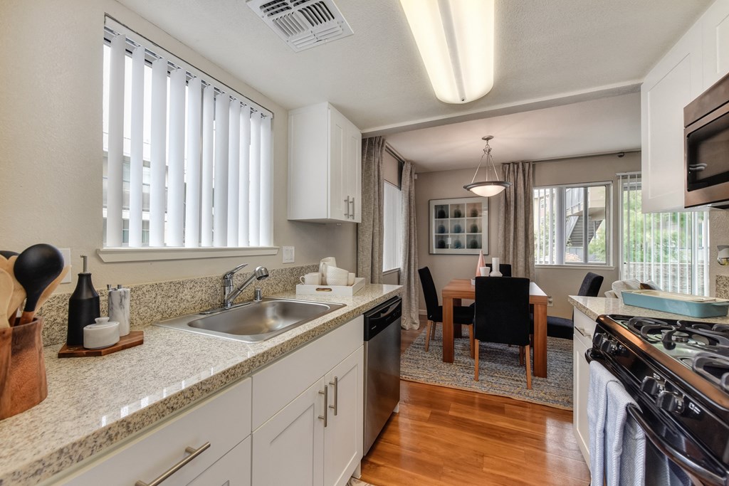 Kitchen with View of Dining Room with Wood Inspired Floor, Sink, Cupboards, Stove, Oven, Wooden Dining Room Table and Black Chairs at Addison Ranch Apartments, Petaluma, CA
