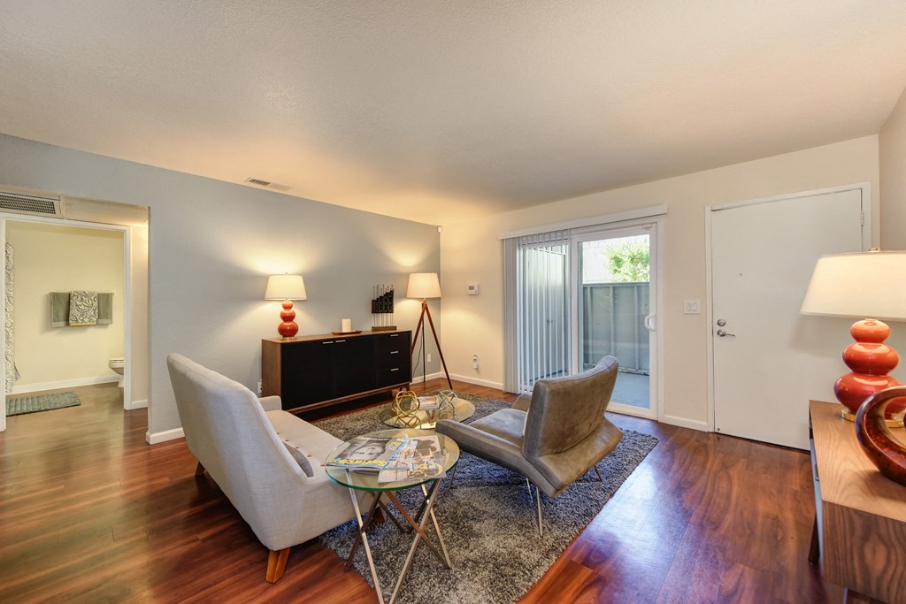 Model home living room with hardwood inspired flooring and views of the sliding glass door to patio and the front door. at Monte Bello Apartments, California