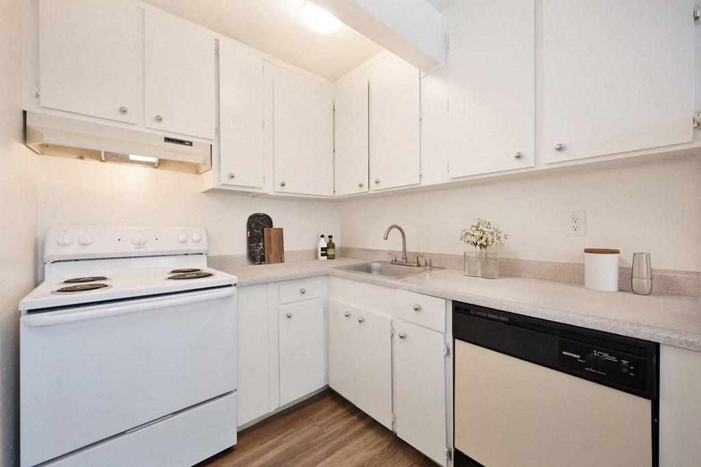 A white kitchen with a stove, sink, and cabinets. at Olympus Park Apartments, Roseville, 95661