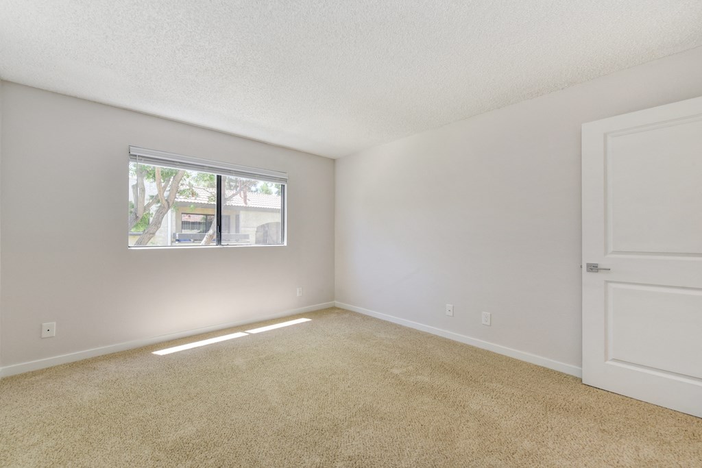 A vacant apartment bedroom with carpet and a window with blinds.