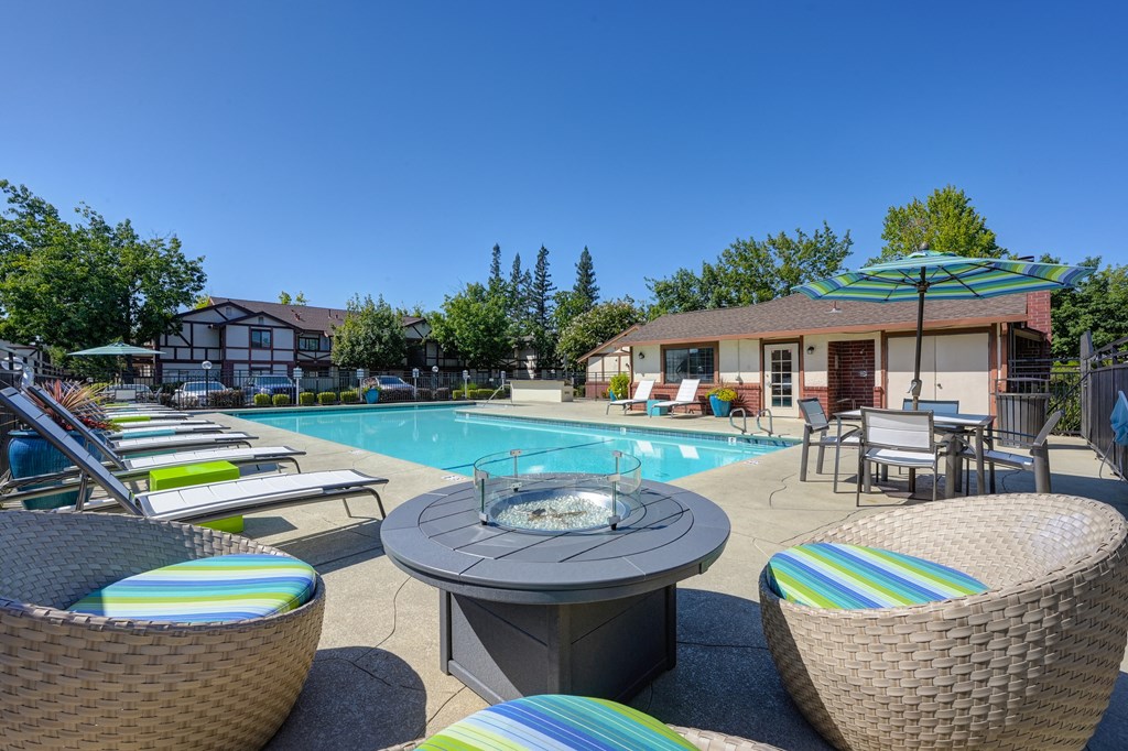 Swimming pool area with chaise lounge chairs, umbrellas, tables and gas firepit at Rocklin Manor  Apartments, Rocklin  , California