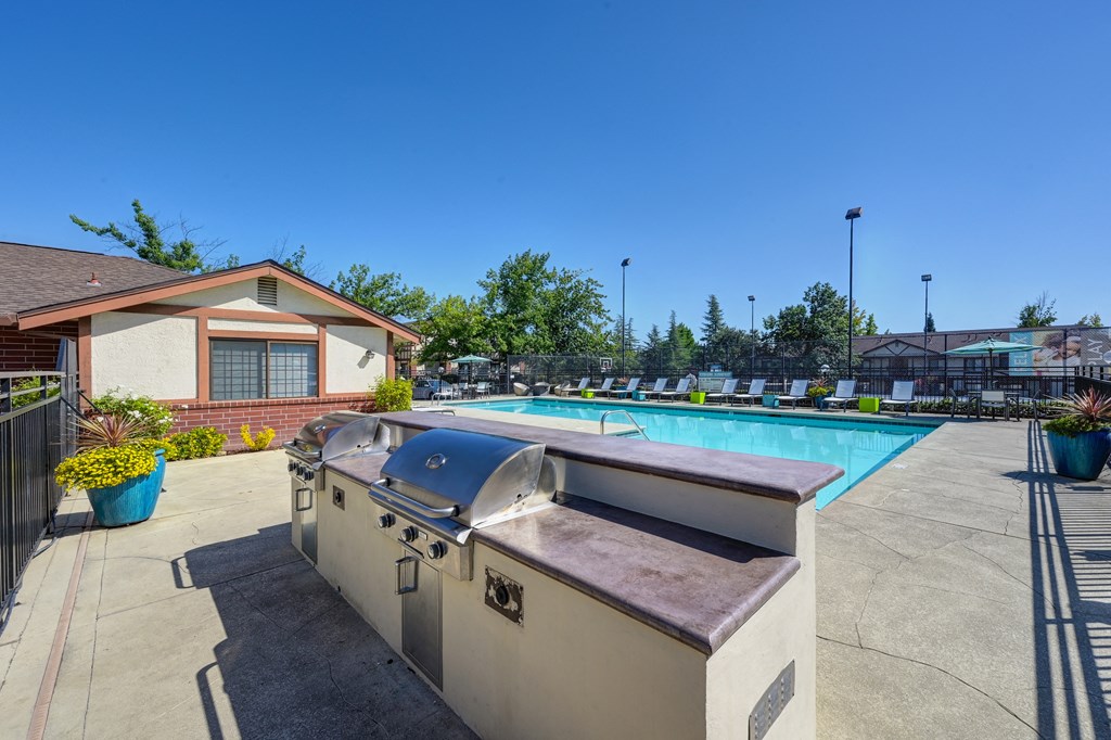 BBQ and Seating Area with Grills, Table, Blue/Yellow Patio Umbrella, Lime Green Chairs and View of Pool at Rocklin Manor  Apartments, Rocklin  