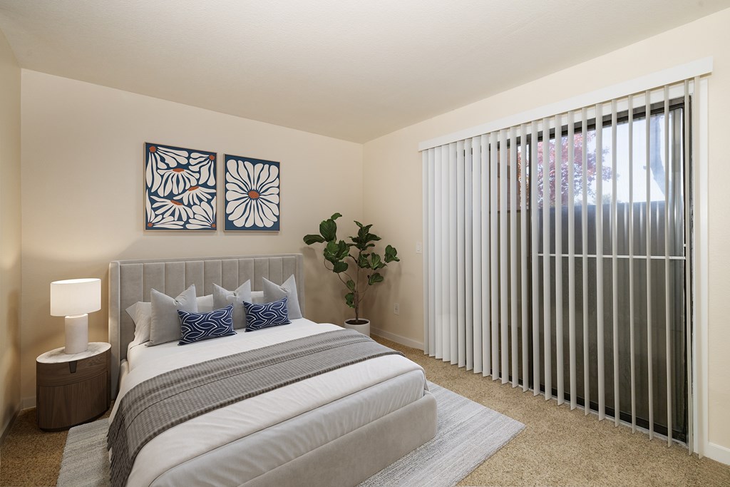 A bedroom with a bed, pillows, a lamp, and a plant.