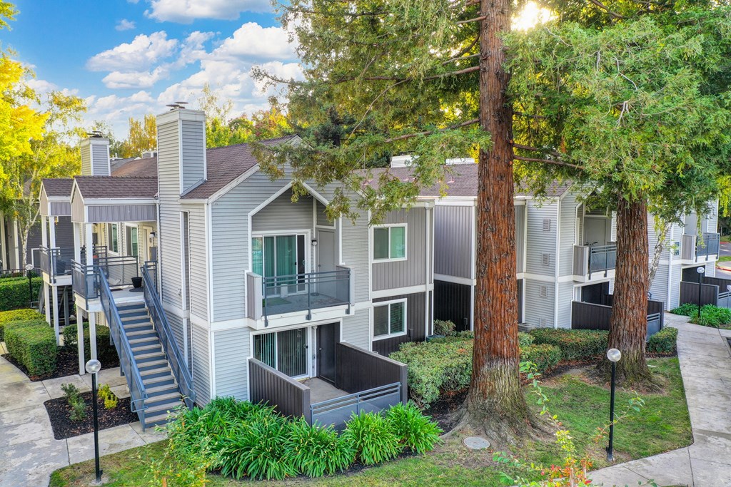 Slight ariel shot of the building exterior with walkway, grass and rees at Rush River Apartments, Sacramento, 95831