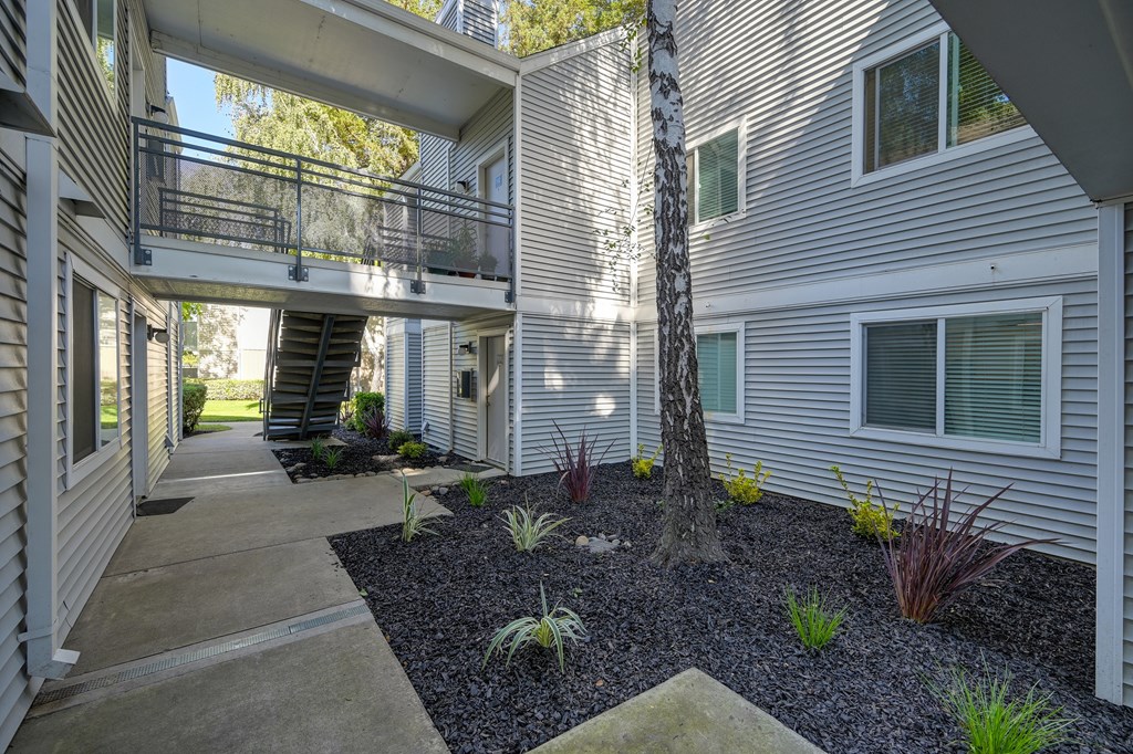 Community walk path in front of a apartment building with a catwalk-like walkway above. at Rush River Apartments, Sacramento
