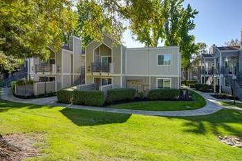 Exterior of the apartment community with large grassy area, mature trees and landscaped bushes. - Photo Gallery 28
