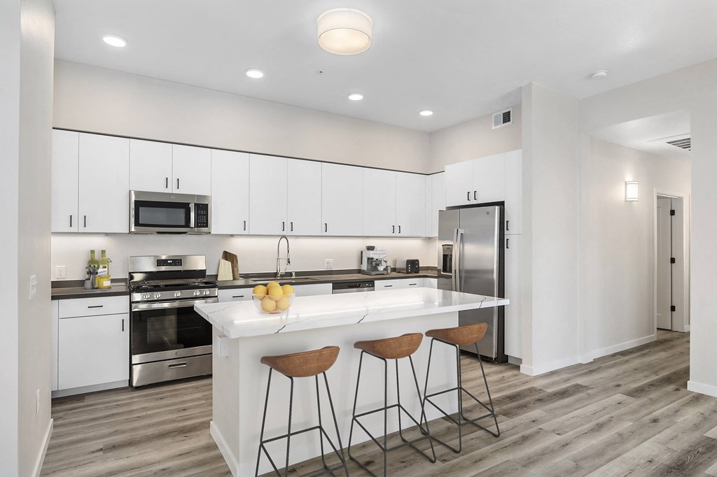 a kitchen with white cabinetry and a large white island with three stools at Sierra Gateway Apartments, Rocklin