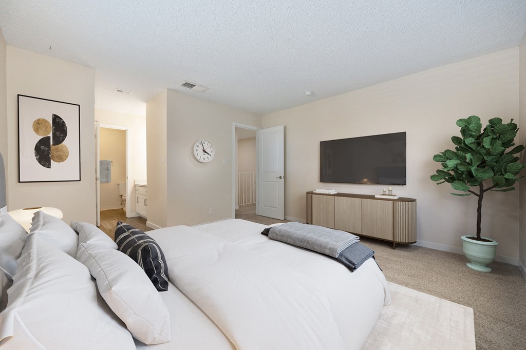 Primary bedroom in the townhouse floor plan with white bed console table and tv on the wall at Silverstone Apartments, Davis, CA