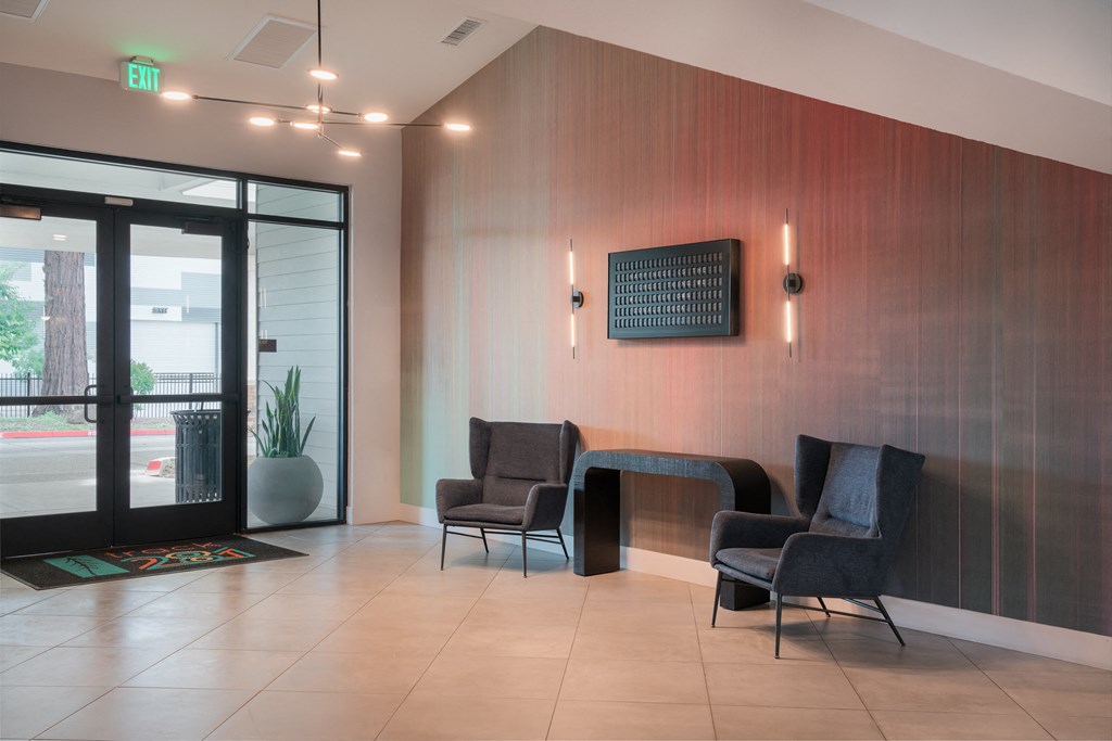 a lobby with chairs and a table in front of a glass door