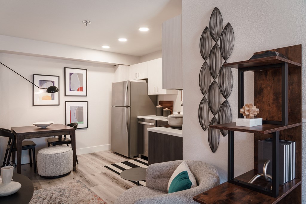 a living room with a couch and a table and a kitchen with a refrigerator