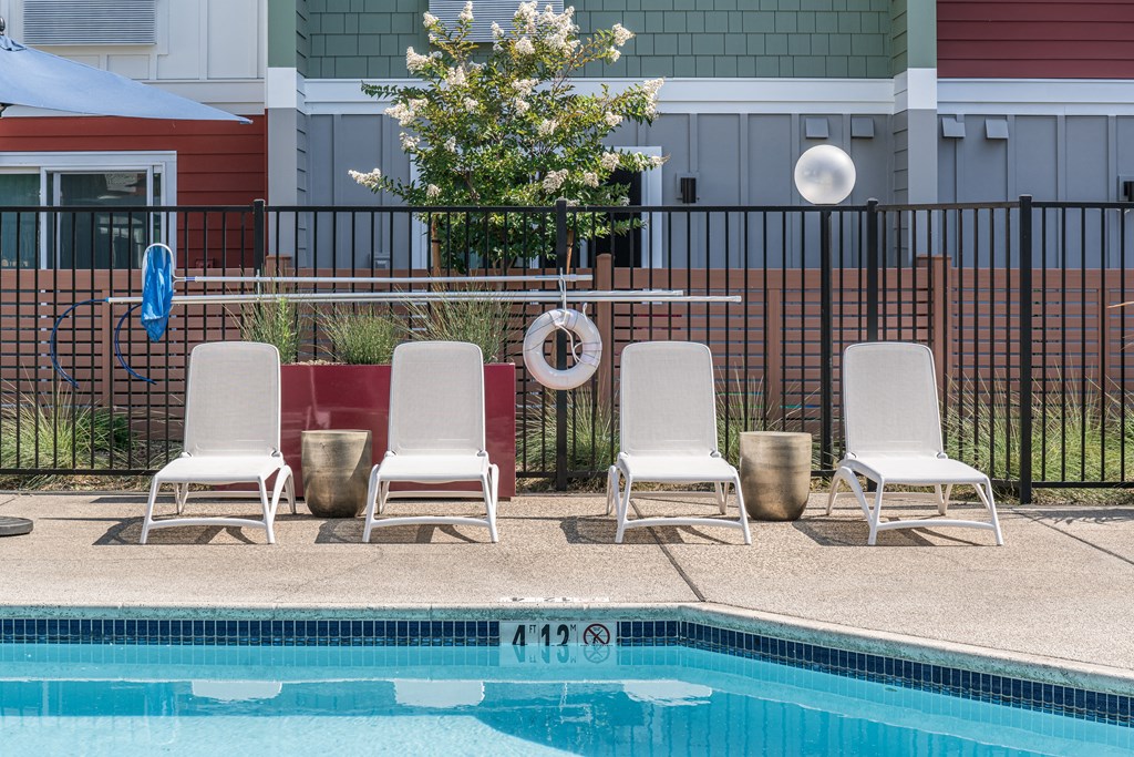 a swimming pool with three white chairs and a poolside umbrella