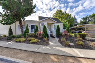 Apartment entrance with small staircase leading up to the front of the building and nice shrubs and tress outside of the building. 