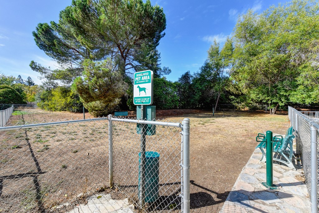 Community gated dog park with pet waste station at entrance and bench inside the fenced area at Vineyard Terrace Apartments, Napa, California