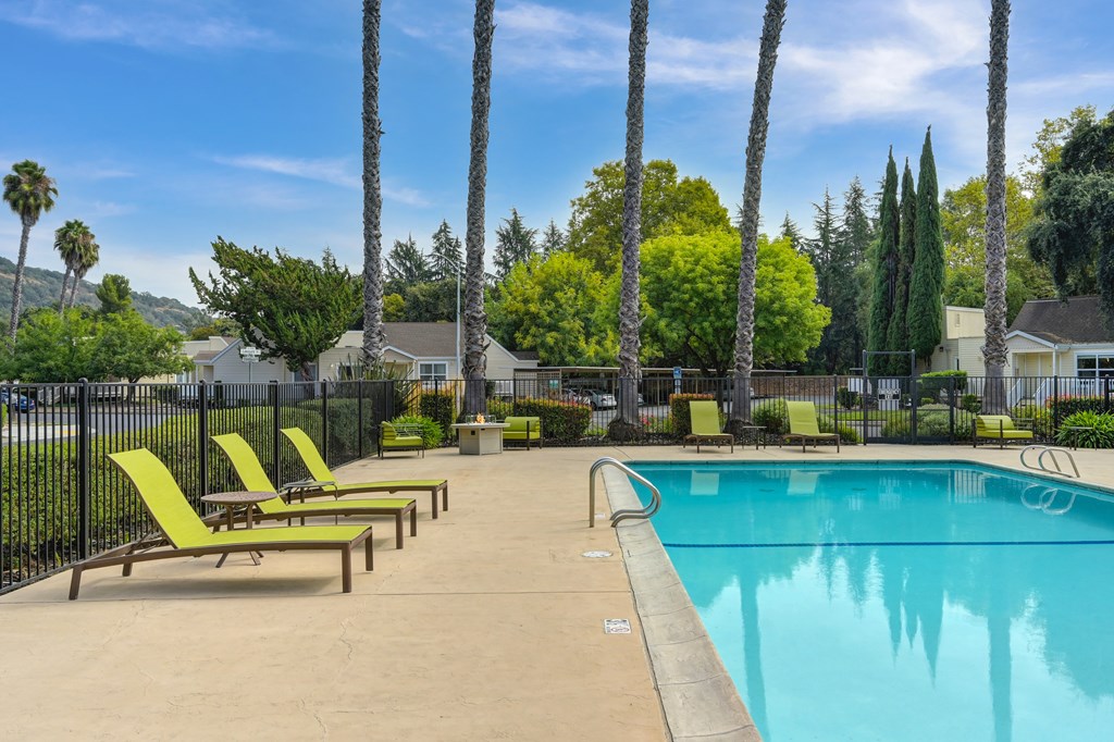 A pool surrounded by palm trees and lounge chairs.