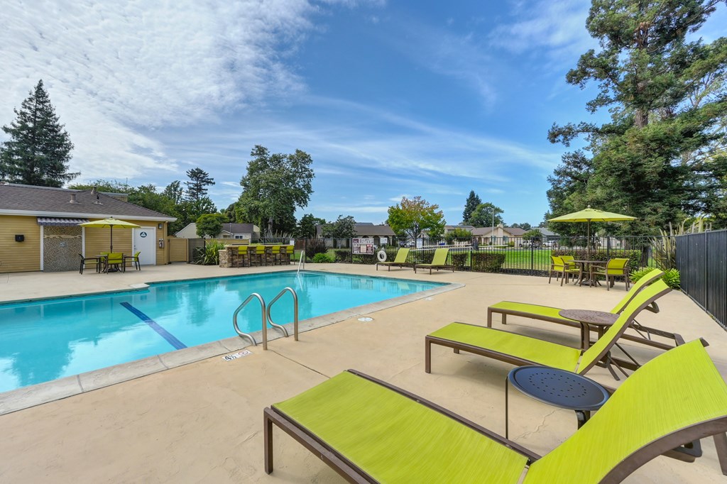 A pool area with sun loungers and a yellow umbrella.
