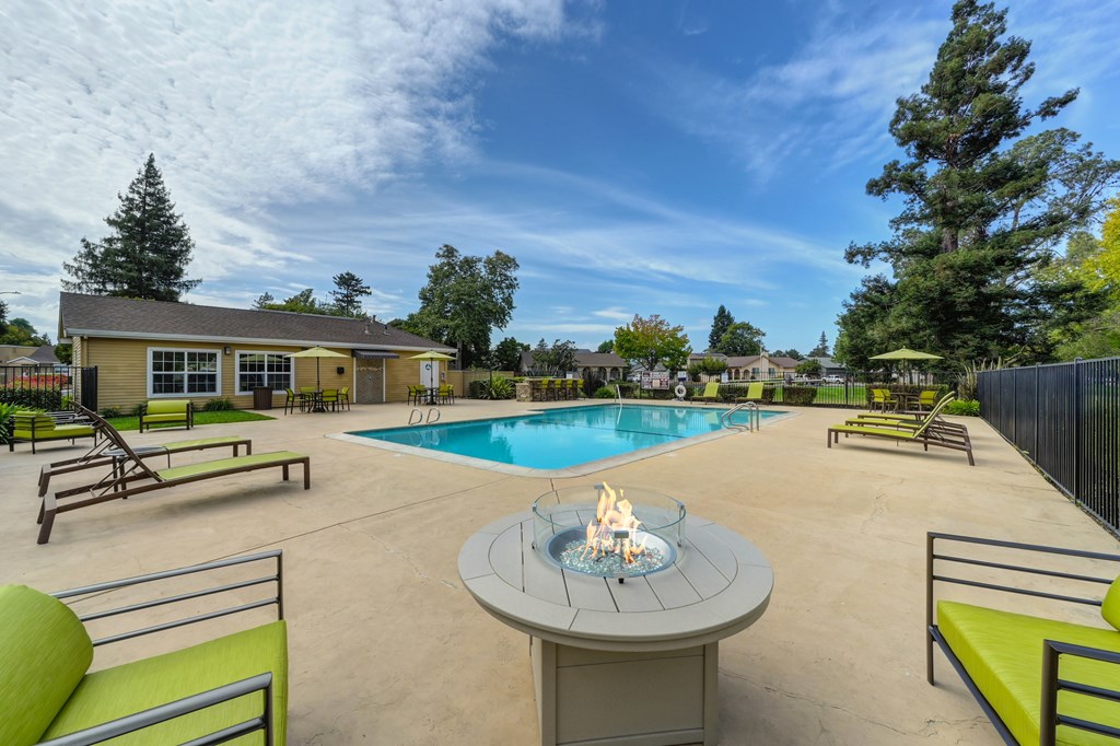 A poolside area with a fire pit in the middle of a concrete patio.