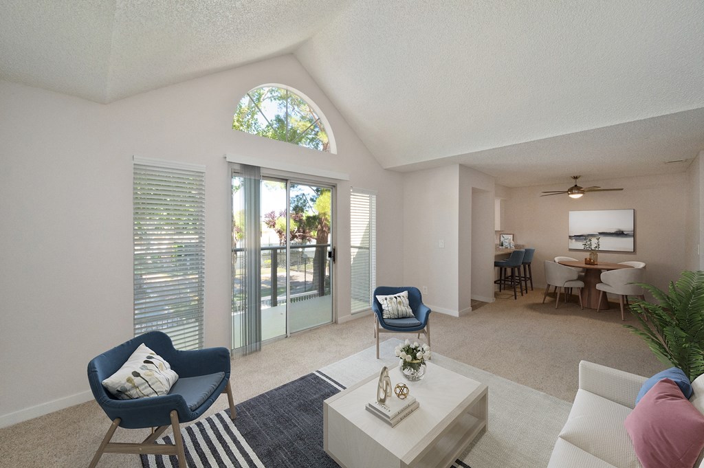 a living room with blue chairs and a white coffee table and a sliding glass door to the private balcony.   Extra rounded windows above the patio door which allow more natural light in.