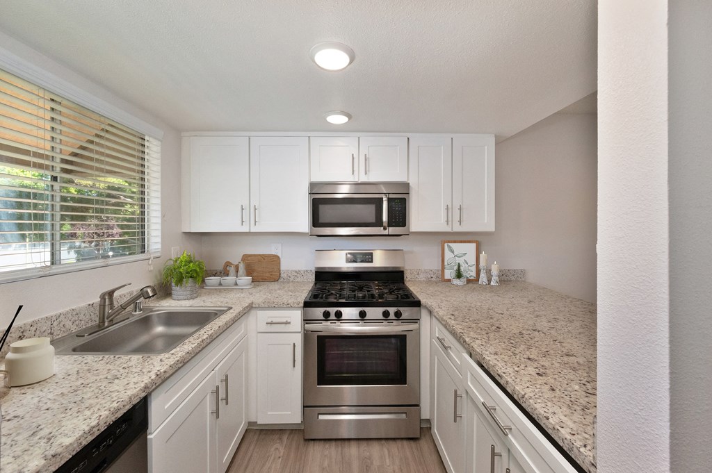 an updated kitchen with granite counter tops and stainless steel appliances.  There is a large window with blinds above the kitchen sink