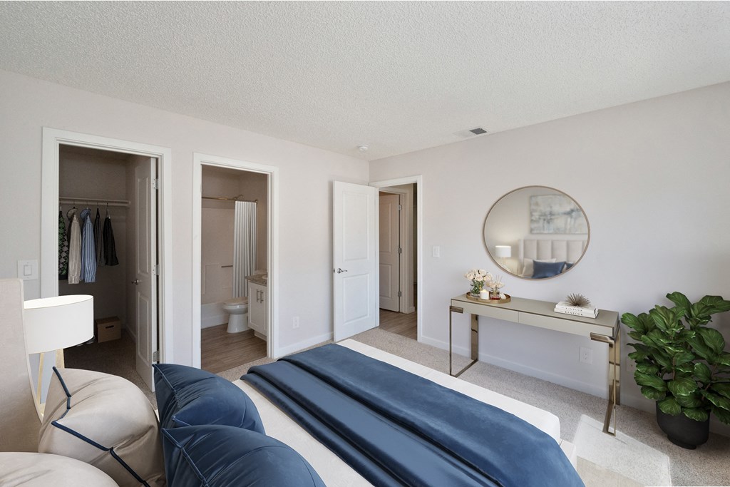 A  bedroom with a bed and a mirror on the wall with both the large extended closet and bathroom attached to the room