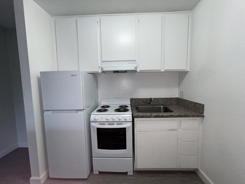 A small kitchen with a white fridge, stove, and cabinets.