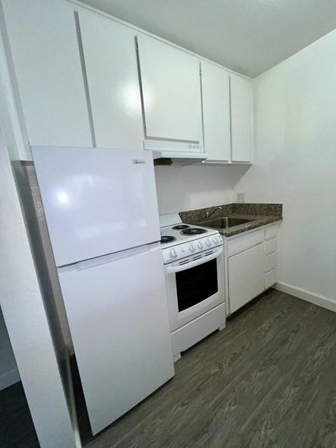 A white fridge and stove in a kitchen with white cabinets.