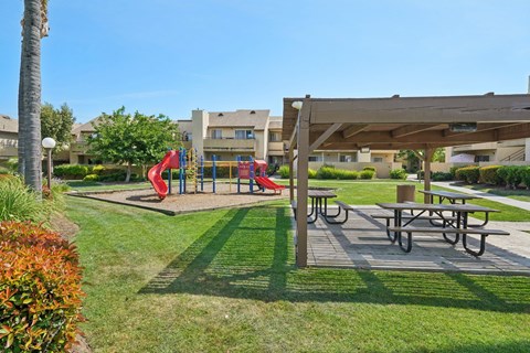 A playground with a red slide and picnic tables.