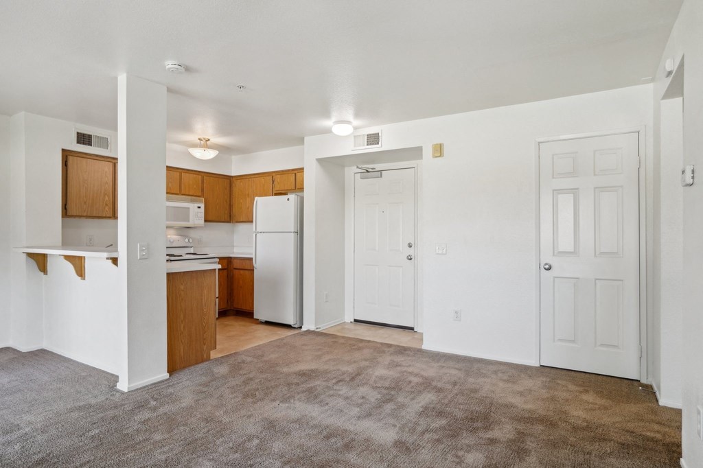 the living room and kitchen of an apartment with white walls and wood cabinets