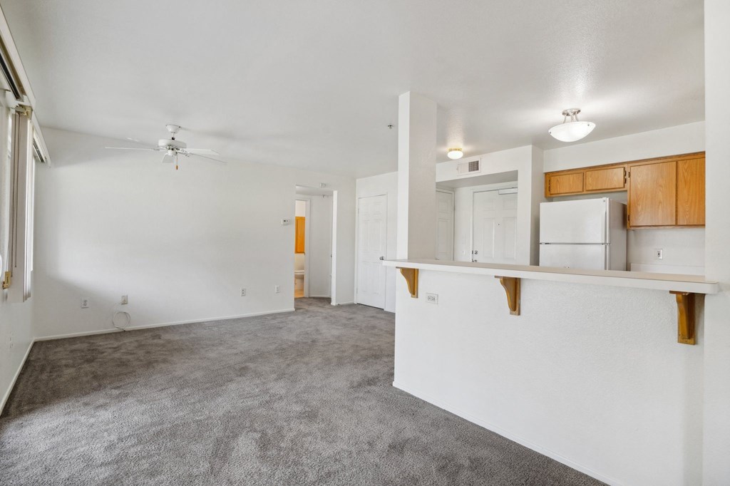 an empty living room with a kitchen and a ceiling fan