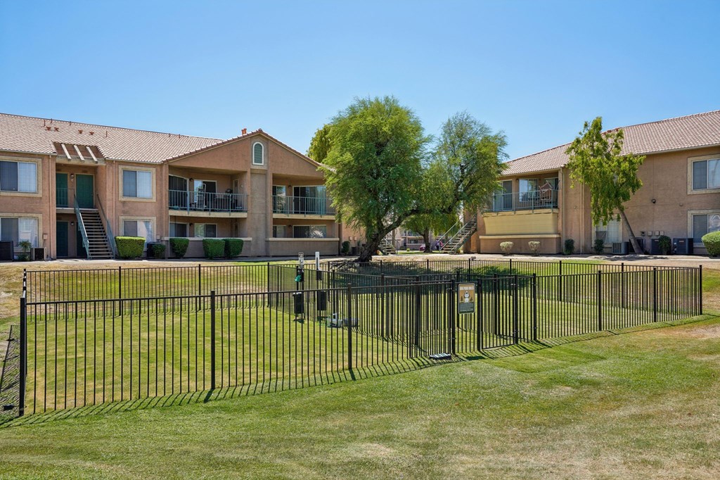 A black fence surrounds a grassy area in front of apartment buildings.